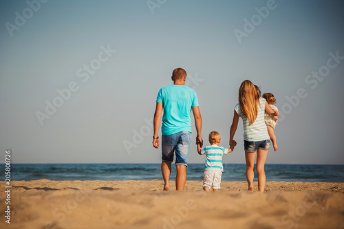Young happy loving family with small kids walking at beach together near the ocean, happy lifestyle family concept. Back view