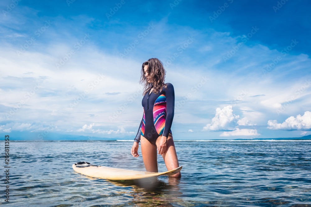 beautiful sportswoman in wetsuit standing at surfing board in ocean at Nusa dua Beach, Bali, Indonesia