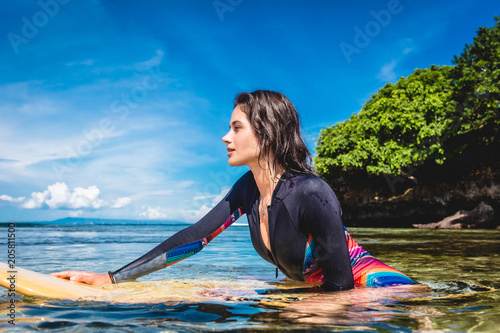 side view of pretty sportswoman in wetsuit on surfing board in ocean at Nusa dua Beach, Bali, Indonesia