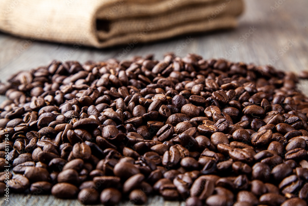 Pile of roasted coffee beans on a wooden table with hessain sack in background Pile of roasted coffee beans on a wooden table with hessain sack in background