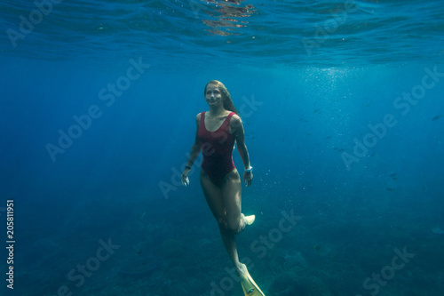underwater photo of young woman in swimming suit and fins diving in ocean alone