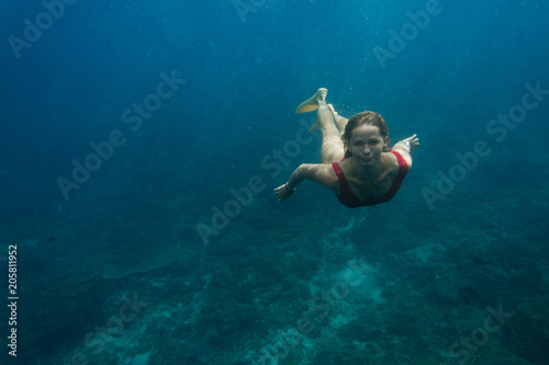 underwater photo of young woman in swimming suit and flippers diving in ocean alone