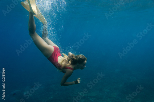underwater photo of young woman in swimming suit and fins diving in ocean alone