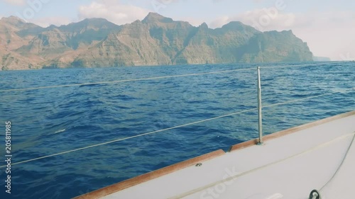 View of cliffy shore of Gran Canaria from board of floating yacht saling in ocean