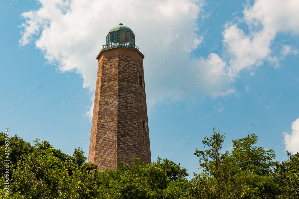 The Old Cape Henry Lighthouse, towers over surrounding trees with a partly cloudy sky on the Fort Story military base.
