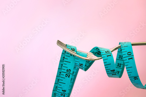 Diet for weight loss , measuring tape with fork on a light pink background for take care healthy eating concept