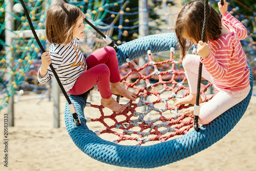 two little girls are swinging on a swing at the playground on a summer day photo