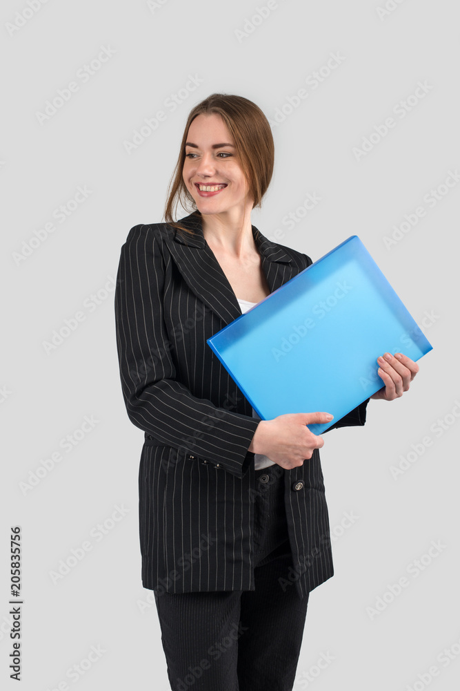 young successful woman in a strict dark suit with a blue folder in hands looking aside and smiling young successful woman in a strict dark suit with a blue folder in hands looking aside and smiling