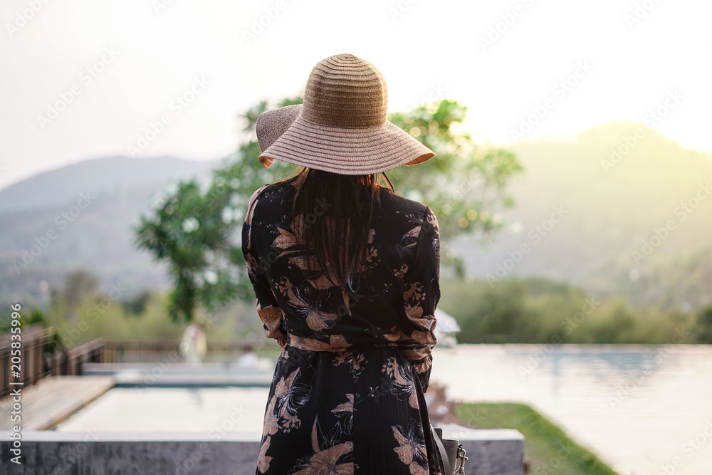 Beautiful attractive woman at the swimming terrace with oversize hat over her eyes, wearing a long dress