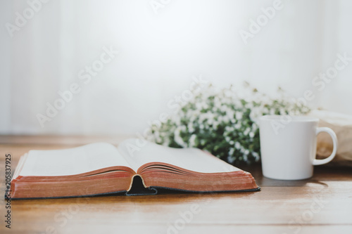 Fotografia, Obraz Holy bible with flowers on wooden table background against window light with copy space