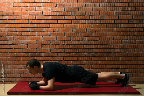 athlete in the hall doing an exercise on a red mat for training a press against a brick wall background