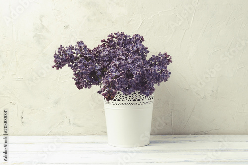 White Decorative Pail Bucket with Lilac on a white stone background and white wooden table. Flat lay, top view