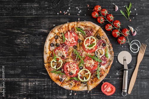 Vegetables, mushrooms and tomatoes pizza on a black wooden background. It can be used as a background