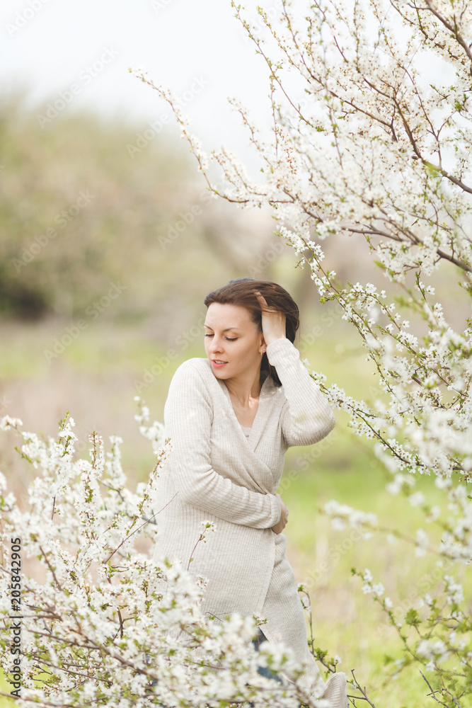 Young relaxed tender charming woman in light casual clothes holding hands folded standing in city garden or park on blooming tree background. Spring nature, flowers. Lifestyle, leisure concept. Young relaxed tender charming woman in light casual clothes holding hands folded standing in city garden or park on blooming tree background. Spring nature, flowers. Lifestyle, leisure concept.