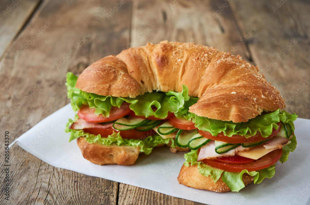 Croissant sandwich with tomatoes, cucumbers, bacon, cheese and lettuce on a wooden table Croissant sandwich with tomatoes, cucumbers, bacon, cheese and lettuce on a wooden table