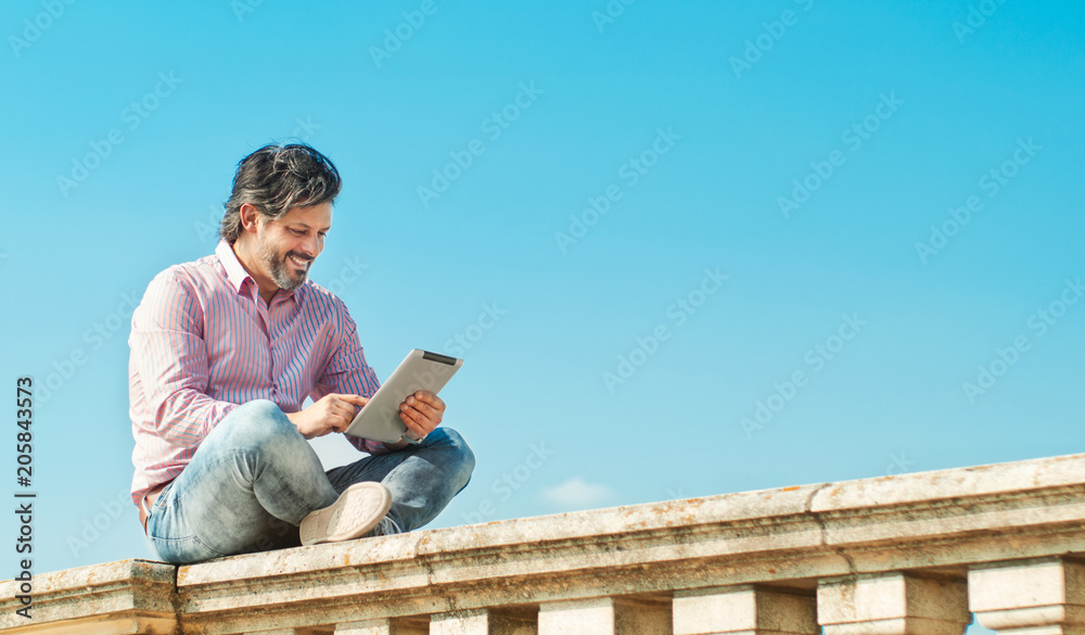Joyful bearded man with digital tablet outdoors browsing to his wife Joyful bearded man with digital tablet outdoors browsing to his wife