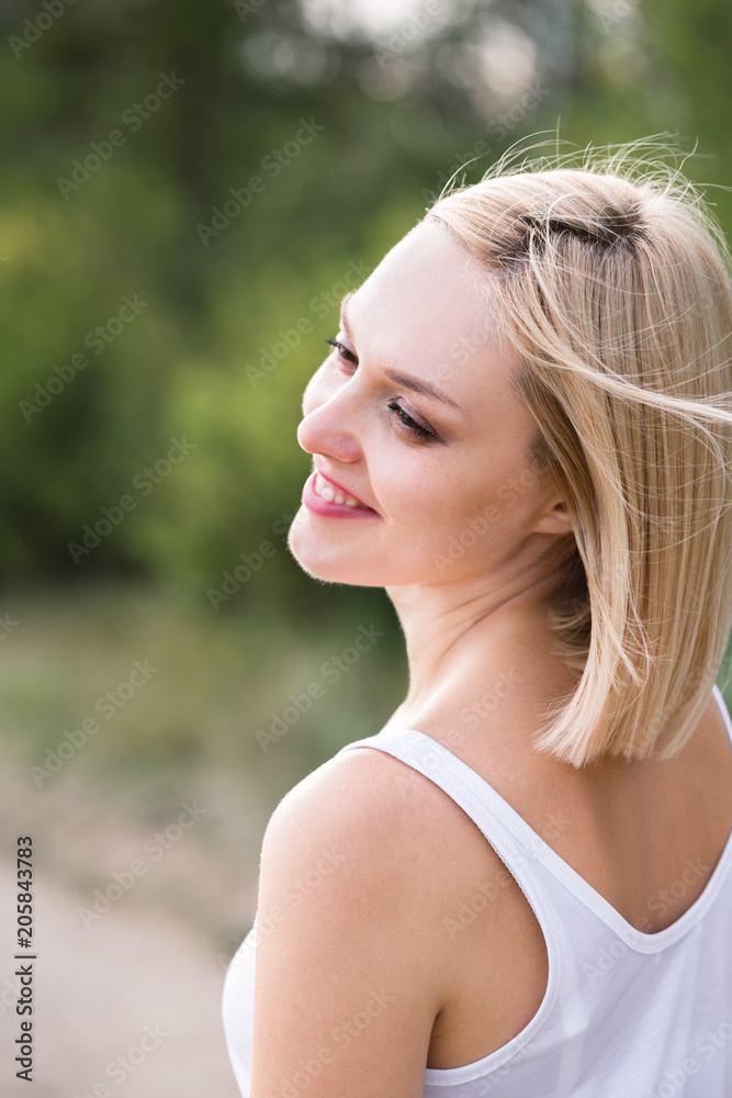 Outdoor portrait of a beautiful smiling middle aged blonde woman in white.