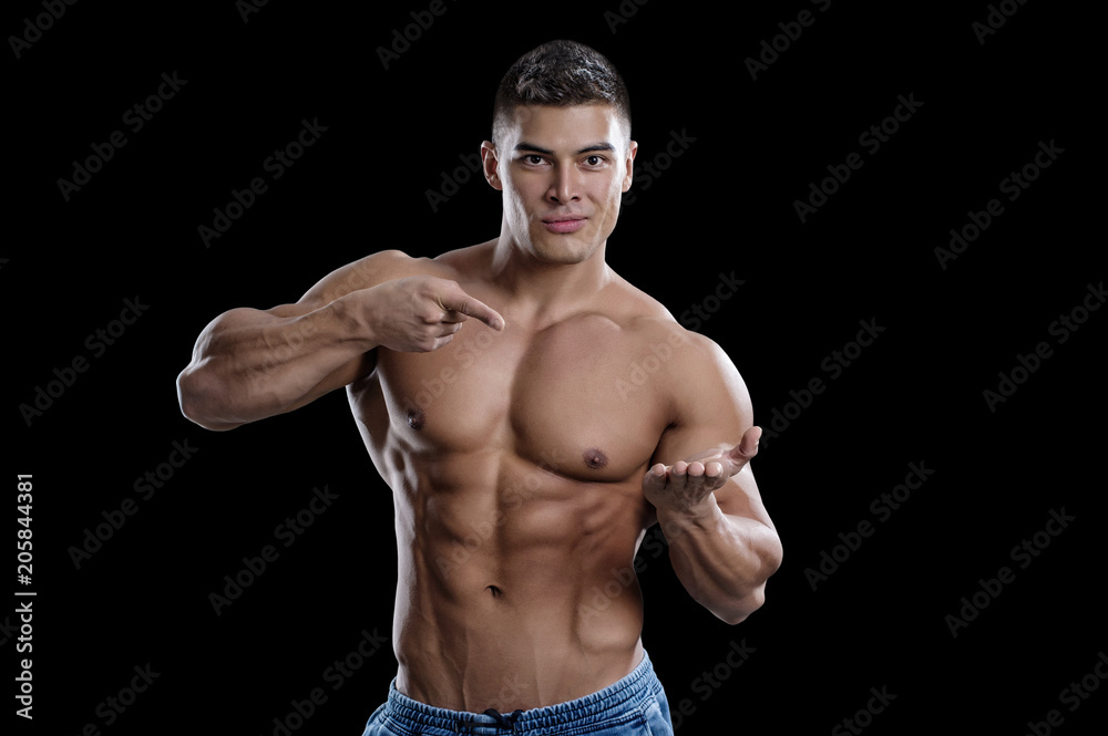 A smiling male bodybuilder points to his open palm. The picture is suitable for advertising sports goods and services. Isolated in black background. A smiling male bodybuilder points to his open palm. The picture is suitable for advertising sports goods and services. Isolated in black background.