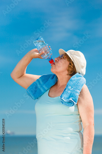 old woman drinking mineral water in plastic bottle outdoor