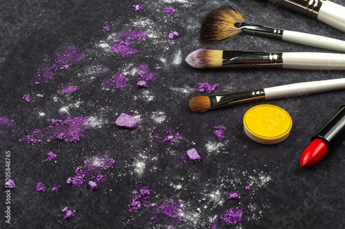 brushes, lipstick and purple loose eye shadows lying on a black background. concept of professional make up artist tools. free space for advertising photo