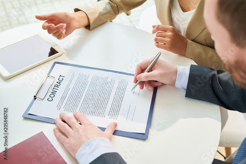High angle closeup of businessman signing contract during meeting with unrecognizable businesswoman sitting beside him explaining terms of deal