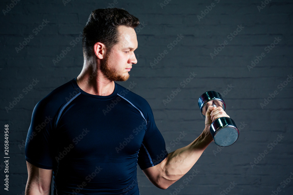 young and handsome athlete man doing exercises for the muscles of the hands of dumbells in the gym. Crossfit and concept of health