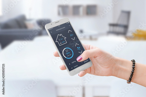 Woman hold smart phone and use smart home control app to monitoring home parameters.