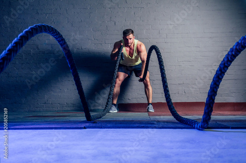 young and handsome male athlete man doing exercises for the muscles of the body with a battle ropes ( rope ) in fitness gym. concept of a healthy lifestyle and crossfit photo