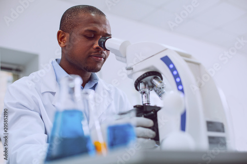 I adore biology. Concentrated professional biologist working with his microscope and wearing a uniform