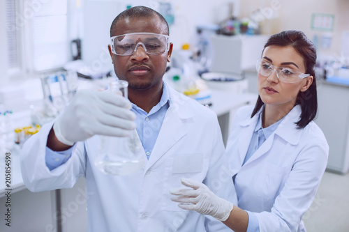 Team spirit. Determined afro-american biologist conducting a test and his colleague helping him