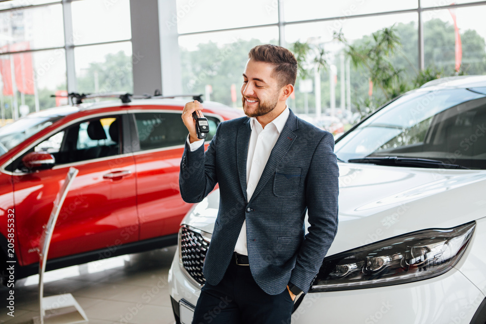 Man is holding a key of their new car, looking at camera and smiling. Man is holding a key of their new car, looking at camera and smiling.