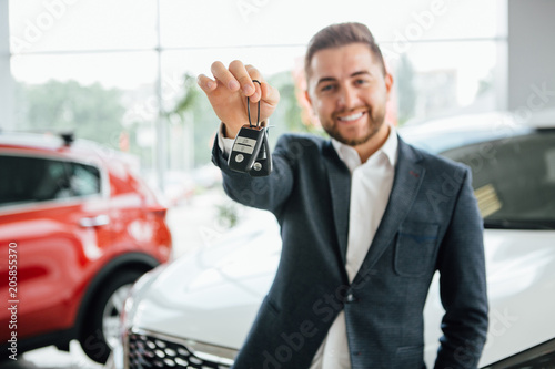 Man is holding a key of their new car  looking at camera and smiling.