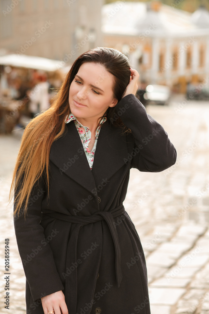 Adorable brunette model with long hair wearing trendy blue coat and cotton shirt posing at sunny day