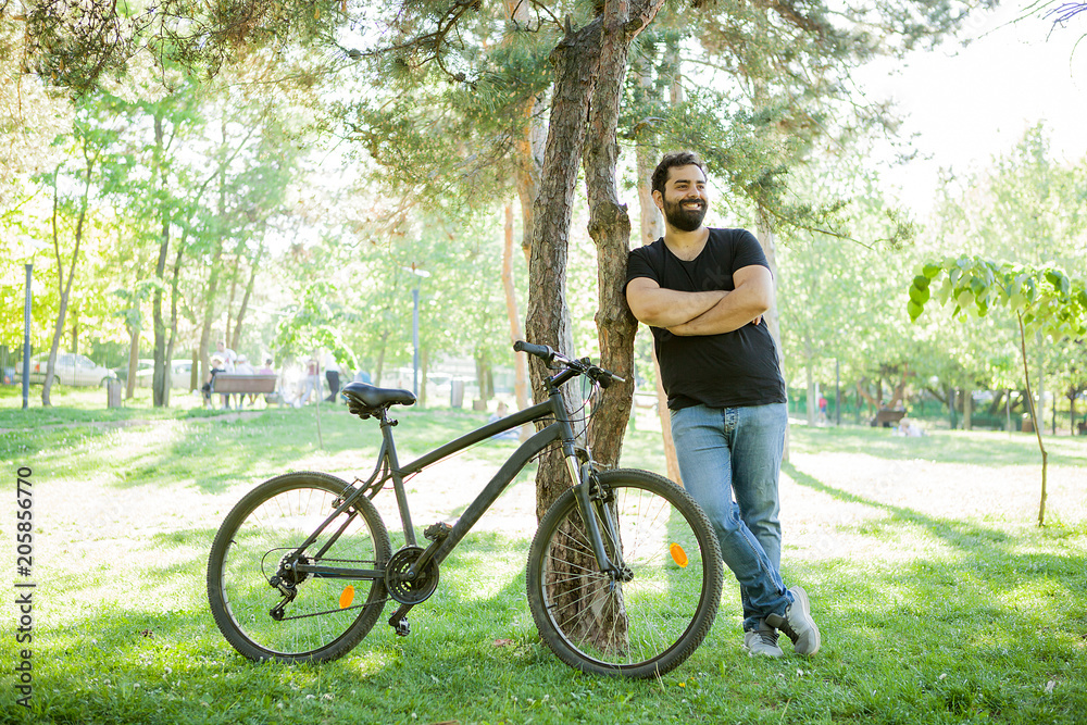 Smiling man leaning on a tree in the park with his bicycle next to him Smiling man leaning on a tree in the park with his bicycle next to him