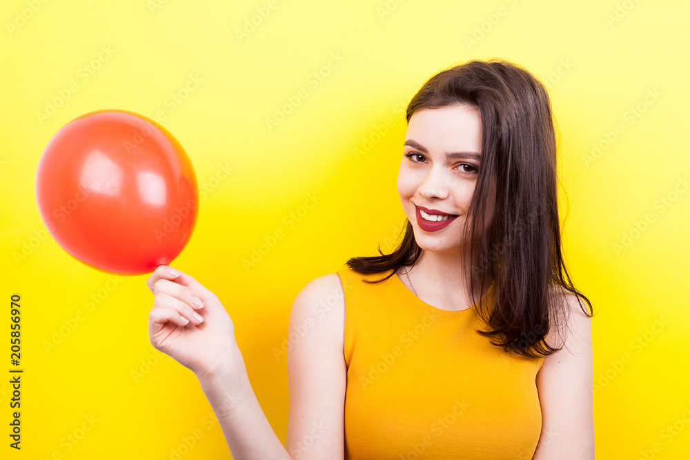 Smiling beautiful woman playing with a red balloon on yellow background Smiling beautiful woman playing with a red balloon on yellow background