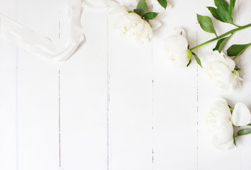 Styled stock photo. Feminine wedding table composition with white peonies flowers and silk ribbon on old white wooden background. Empty space. Top view. Picture for blog.