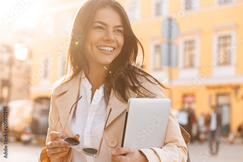 Obraz na plátně Happy brunette woman in jacket holding laptop computer