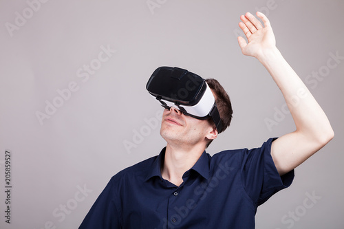 Excited man experiencing virtual reality for the firts time. He is wearing a VR headset. Gray background. Studio photo