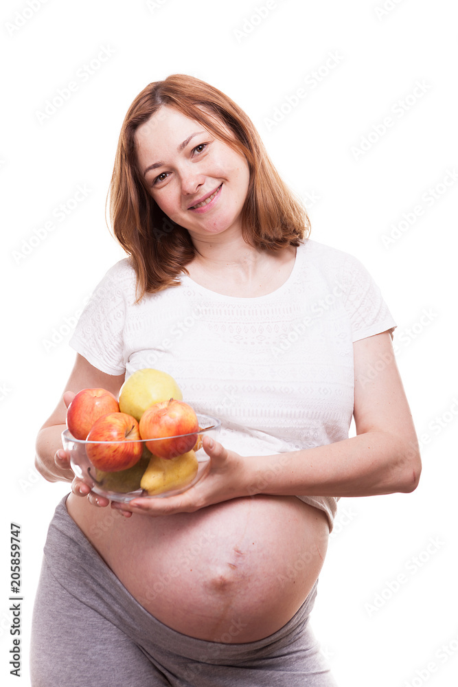 Pregnant woman smiling to the camera and holding a glass bowl with fruits in her hands isolated over white background Pregnant woman smiling to the camera and holding a glass bowl with fruits in her hands isolated over white background