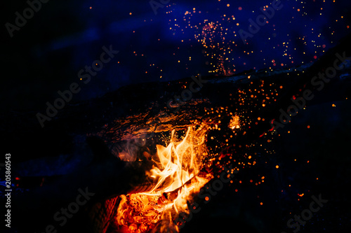 Burning wood at night. Campfire at touristic camp at nature in mountains. Flame amd fire sparks on dark abstract background. Cooking barbecue outdoor. Hellish fire element. Fuel, power and energy.