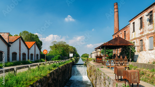 Old industrial warehouses alongside a cascade on a lock at the Naviglio Pavese, a canal that connects the city of Milan with Pavia, Italy.