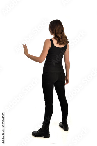 full length portrait of brunette girl wearing black singlet, jeans jeans and boots. standing pose, with back view. isolated on white studio background.