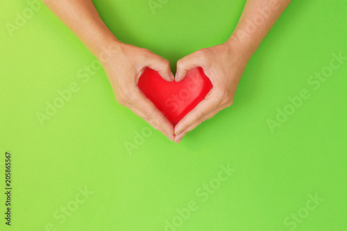 Female hands in shape of heart. With red heart inside on green background. Healthcare and chirty concept.