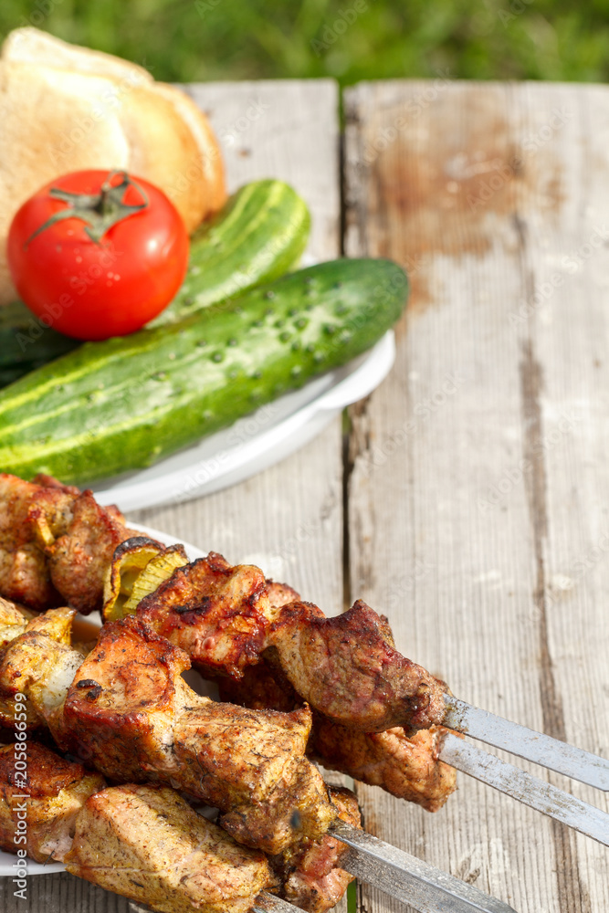 shish kebab on skewers. On a wooden table with fresh vegetables. kebab on the background of green grass