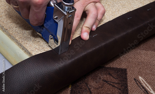 Craftsman fastening leather to the paricle board using staples and stapler photo