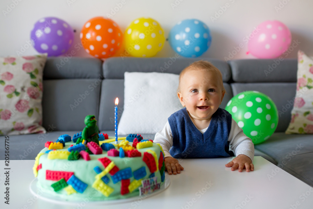 Obraz premium Cute child, baby boy, celebrating his first birthday with colorful cake, candles, balloons