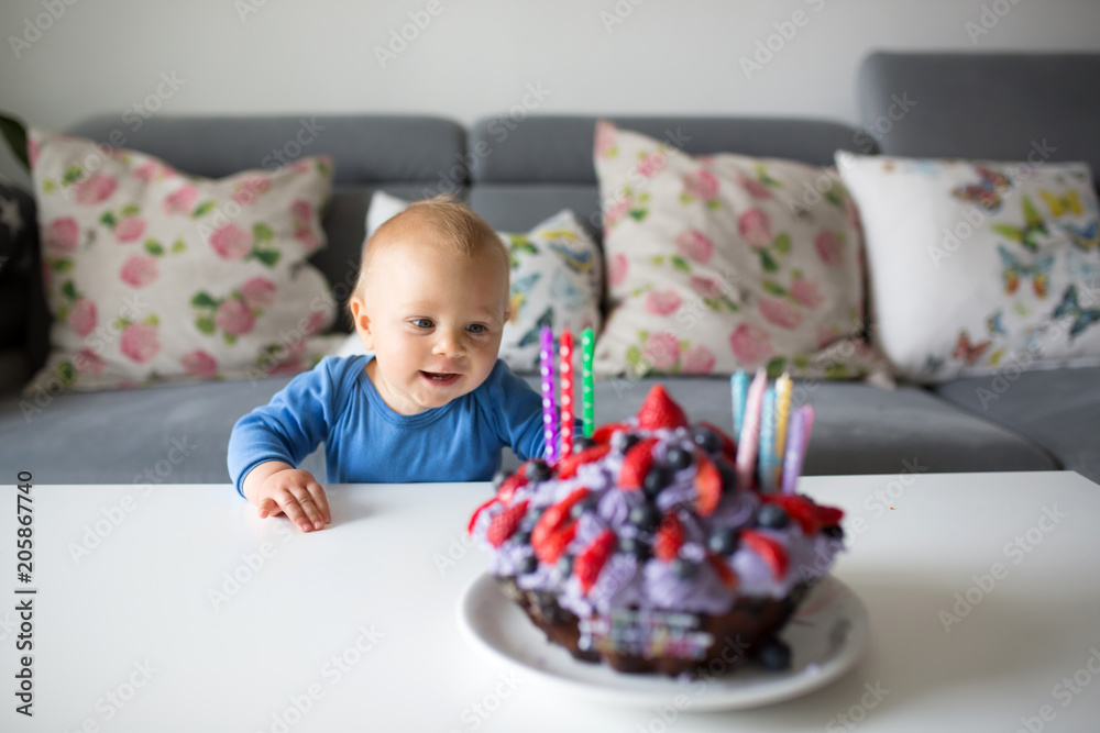 Cute little baby boy, standing next to table with big cupcake cake with cream and candles Cute little baby boy, standing next to table with big cupcake cake with cream and candles
