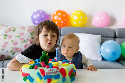 Cute baby child and his older brother, boys, celebrating his first birthday with colorful cake, candles, balloons