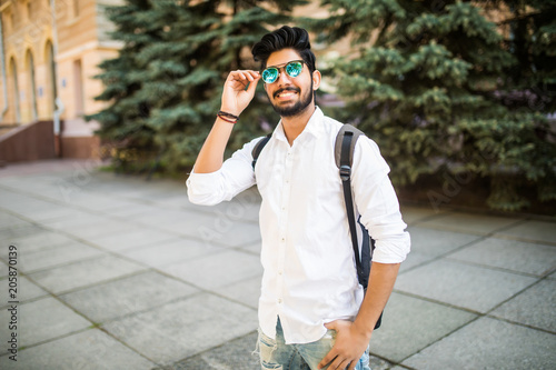 Young handsome Indian student man in sunglasses with backpack in the city street
