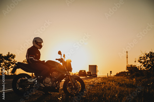 Stunning image of a caucasian bike adventurer sitting near the road in his traveling time resting against sunset.